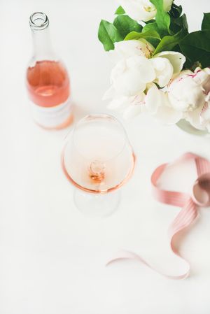 Glass of pink rose wine, and bottle with flowers and ribbon with copy space