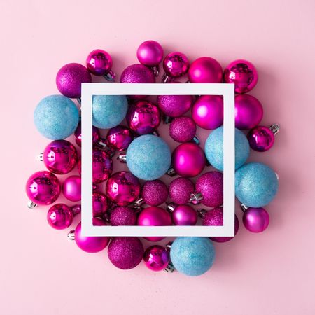 Arrangement of pink and blue festive baubles on pink background with square outline