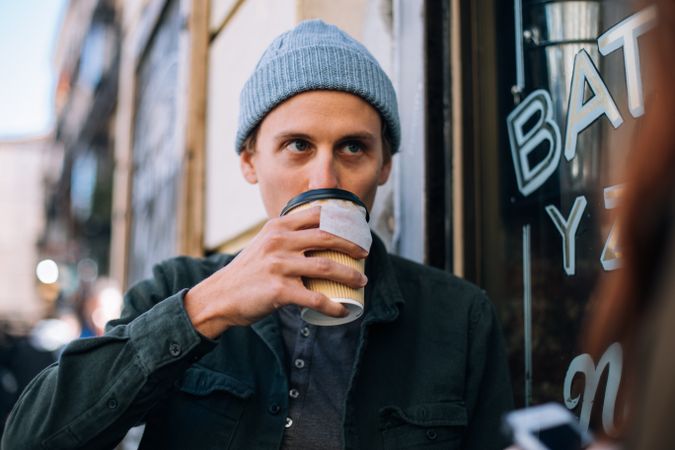 Man drinking a warm drink outside cafe with to go cup