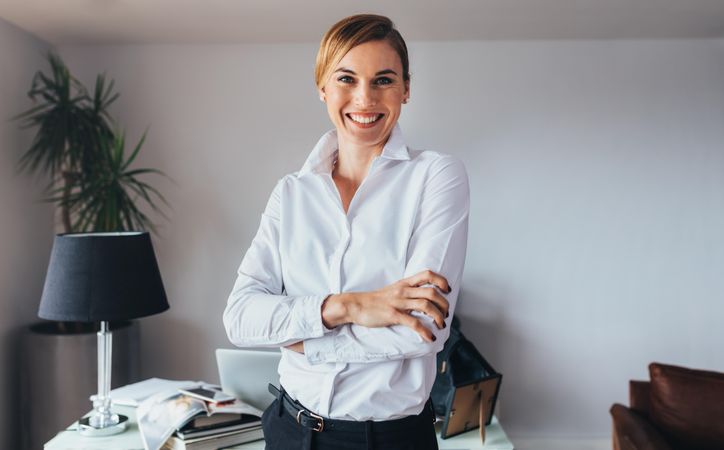 Smiling business woman standing with folded arms in office