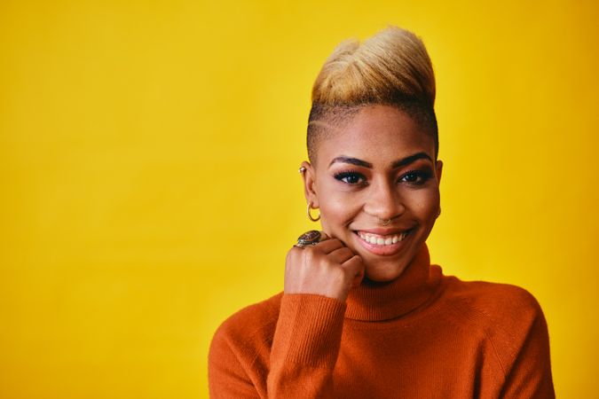 Studio shot of smiling Black woman with short blonde hair in orange sweater with copy space