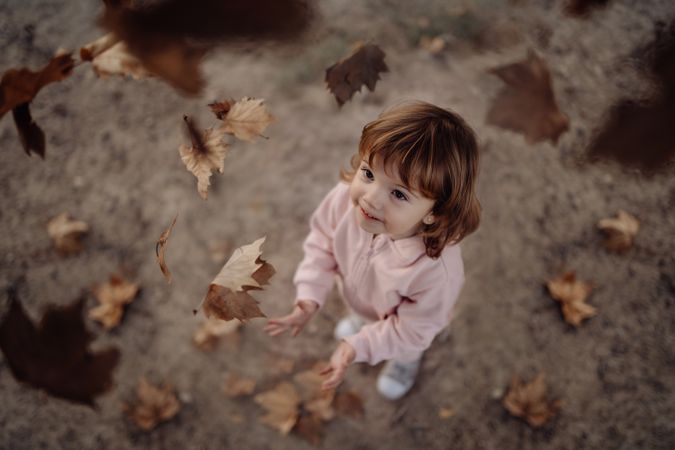 Joyful child scattering leaves on lawn in park