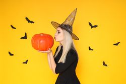 A woman in a wizard's hat kisses a pumpkin, on a yellow background