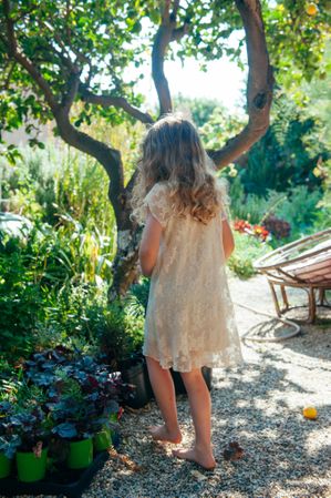 Young girl wearing a dress explores nature while barefoot facing away from the camera
