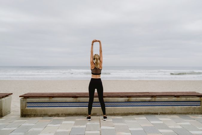 Faceless woman gymnast in sports clothing stretching before exercise at seaside