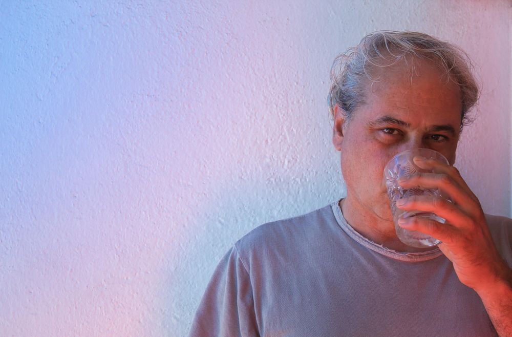 Portrait of middle aged man drinking water against light background in UV lit studio