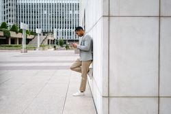 Man using smartphone leaning against wall