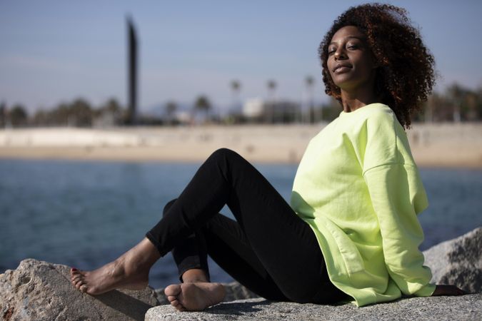 Confident female sitting on coastline in bright green shirt