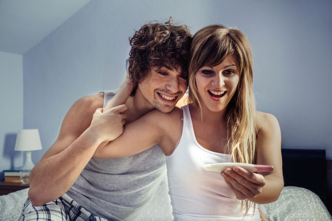 Happy couple looking pregnancy test in bedroom