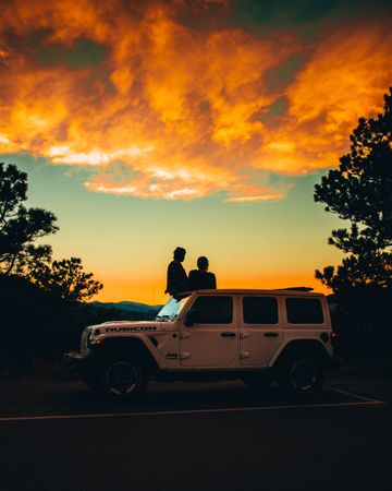 Silhouette of people standing behind a car during sunset