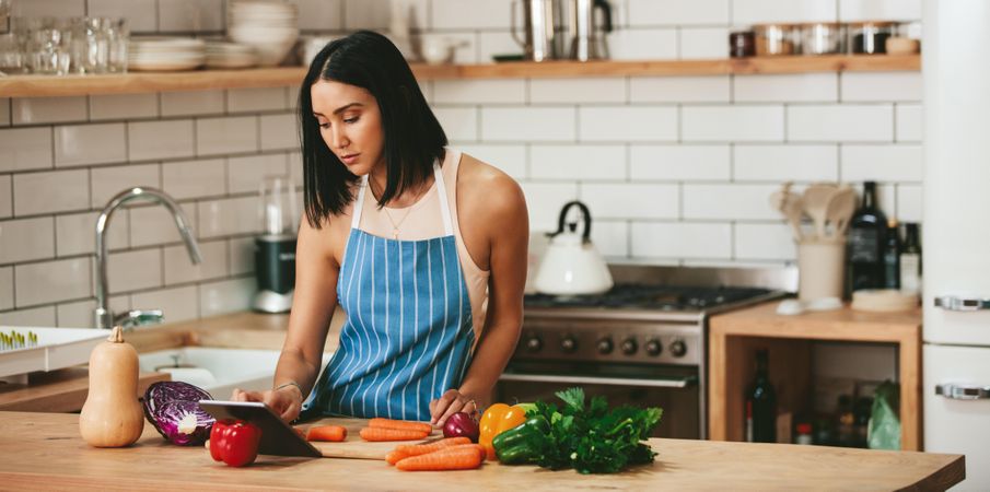 Beautiful woman reading recipe on tablet and preparing ingredients