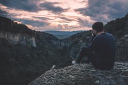 man with photo camera sitting on hill mountain with magnificent sunset