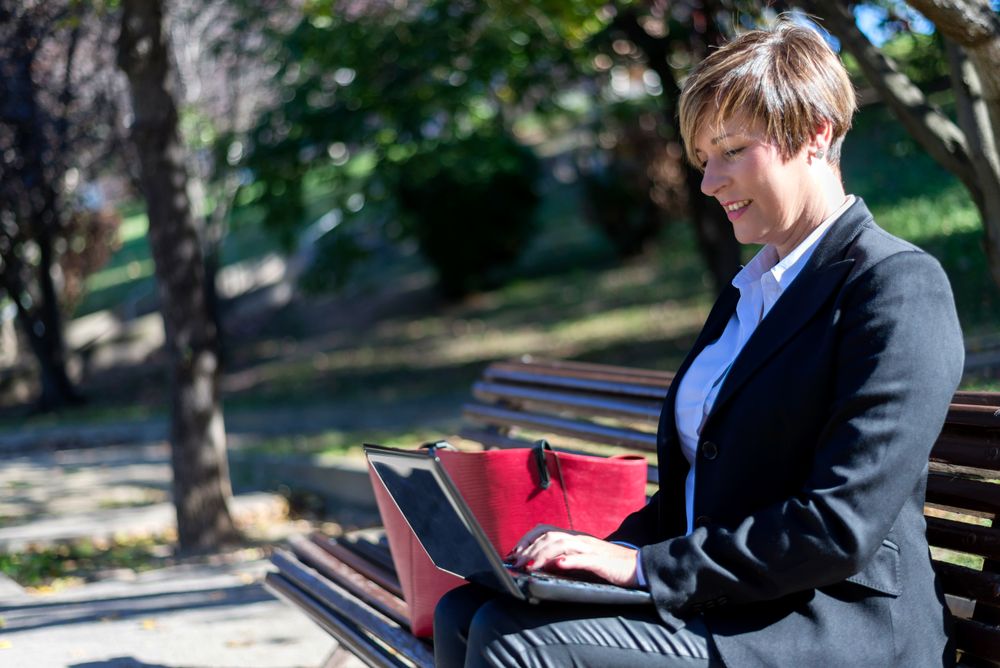 Professional woman sitting on park bench using laptop