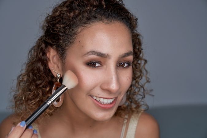 Smiling woman shading blush on cheek with professional brush