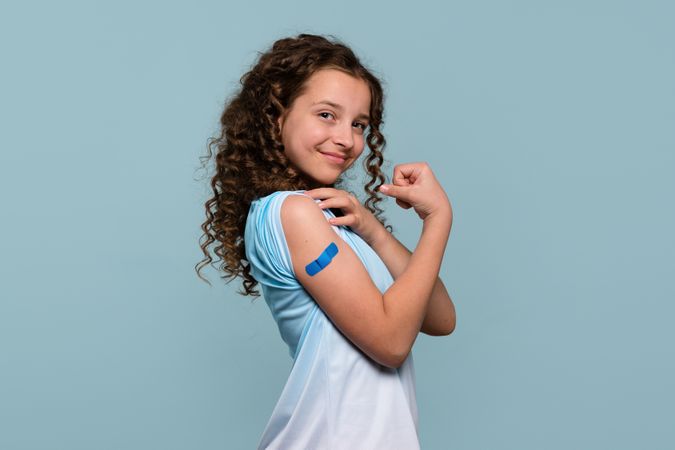 Smiling girl flexing arm with bandage after vaccination.