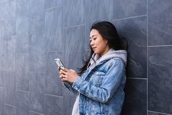 Long hair brunette Asian woman using mobile phone in the street