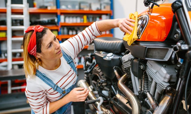 Mechanic woman cleaning motorcycle with cloth and polish on factory