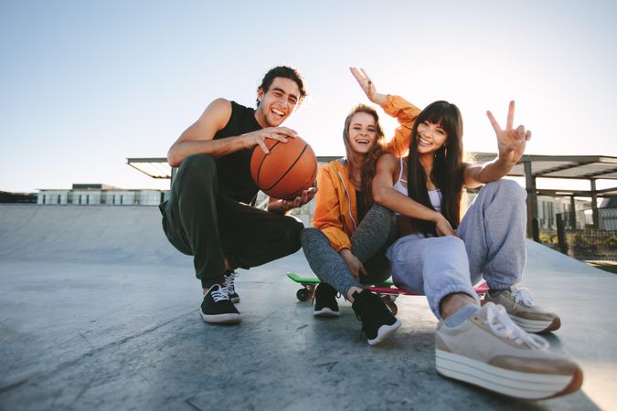 Group of friends sitting at skate park with skateboard and basketball