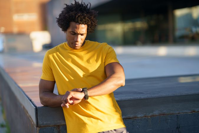 Man in yellow t-shirt checking his smart watch in the sun