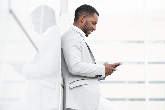 Elegant Black man browsing smartphone leaning on geometrical wall