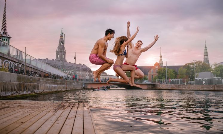 Young friends jumping from jetty into a river in the city