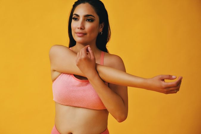 Hispanic female in yoga clothes stretching her arm in yellow studio room