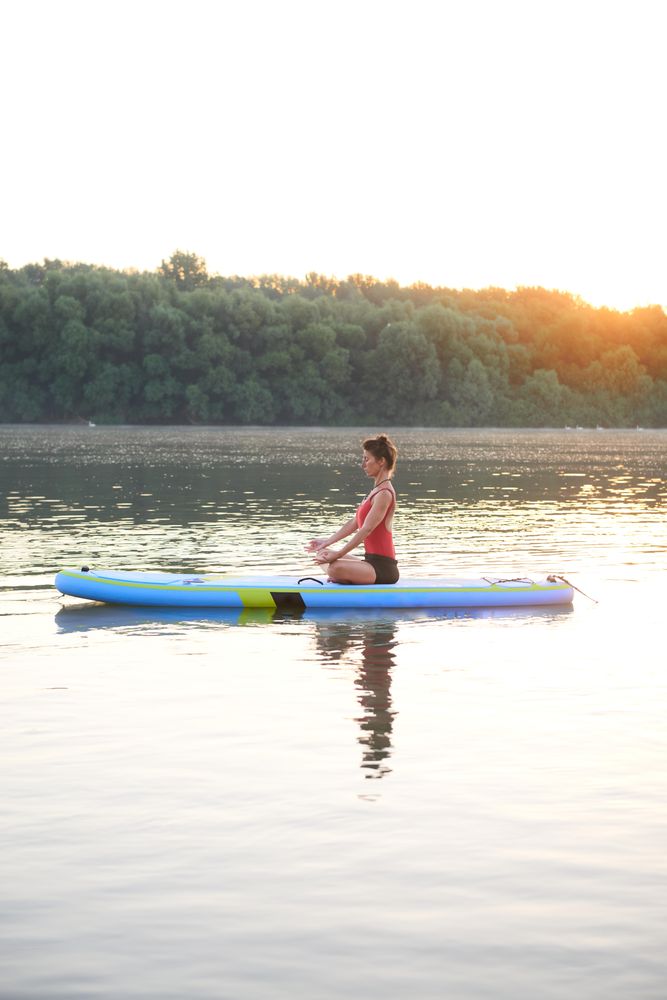 Woman meditating on paddleboard on lake at sunrise