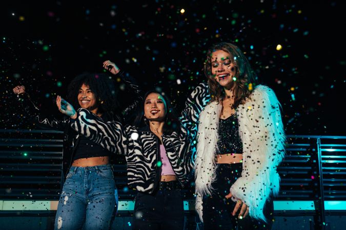 Multi-ethnic group of female friends at party with confetti on city rooftop