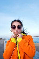 Woman in colorful clothes and sunglasses wearing headphones on the coast