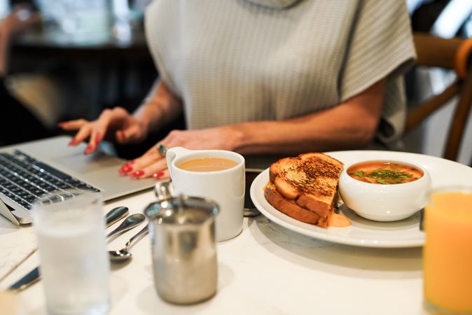 Woman sitting at a table working with food plate and cup of coffee