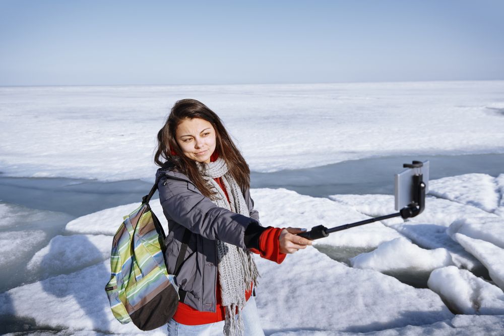 Female traveler outdoors at icy landscape using monopod to make