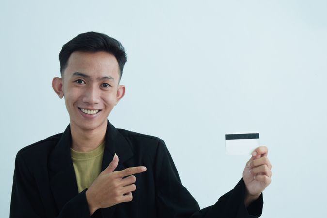 Smiling Asian businessman in suit and tshirt holding white credit card