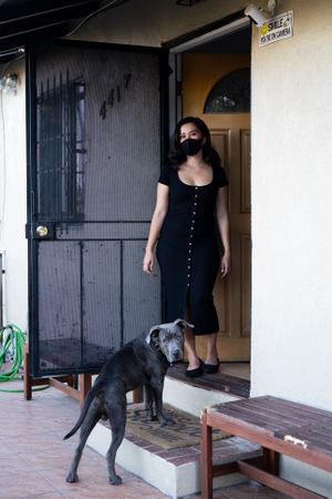 Full length portrait of woman and her dog looking at camera in front of her house
