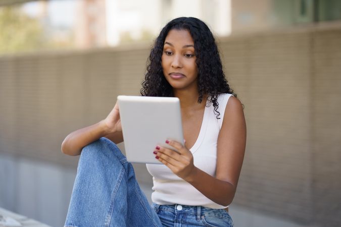 A young woman is actively engaged with her digital tablet while enjoying the outdoor setting