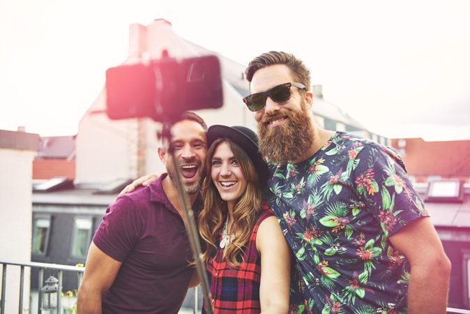 Three people smiling with a selfie stick on a roof