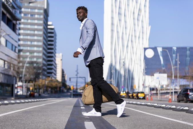 Black man wearing elegant suit crossing the street while looking in the distance in sunny day