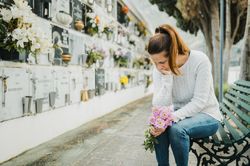 Crying woman witting on bench near grave wall in cemetery