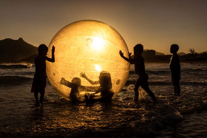 Silhouette of children playing with a huge ball at the Praia da Macumba beach in Rio de Janeiro, Brazil