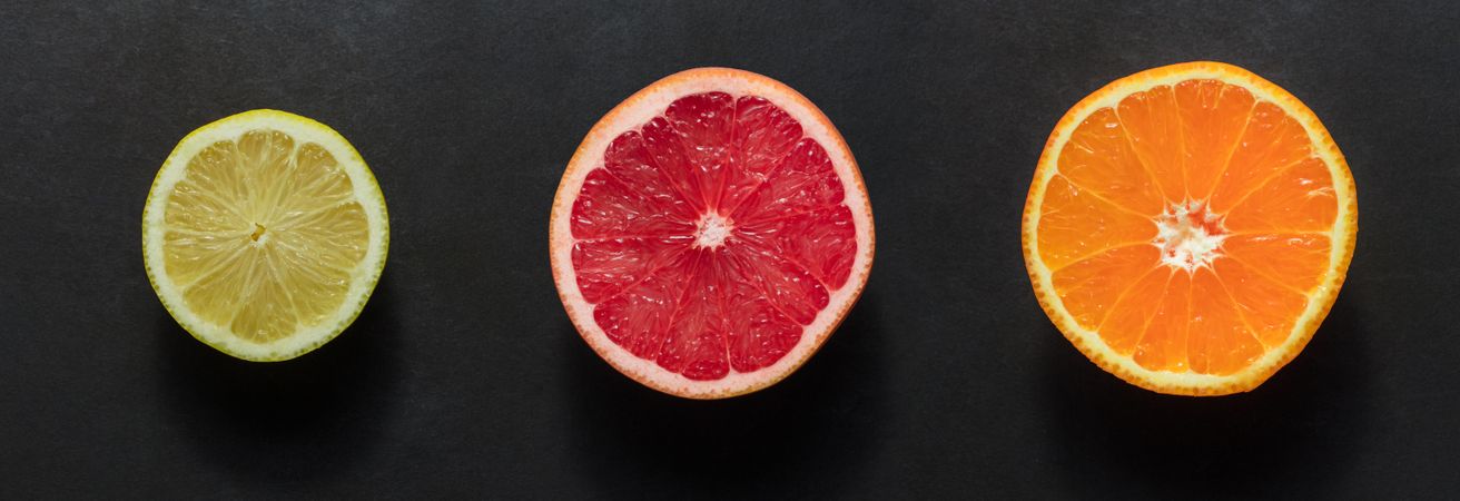 Top view of a half cut orange, grapefruit and a lemon arranged on a dark background
