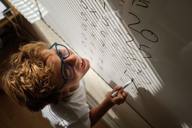 Happy schoolkid writing on whiteboard during math lesson