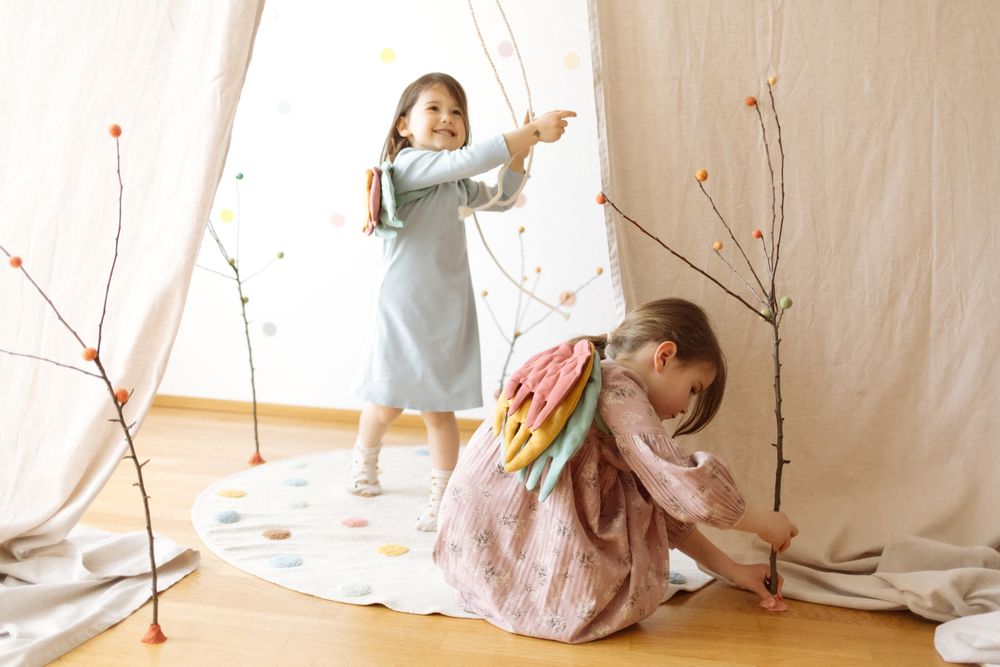 Happy little girls playing with sticks on wooden floor by white curtain