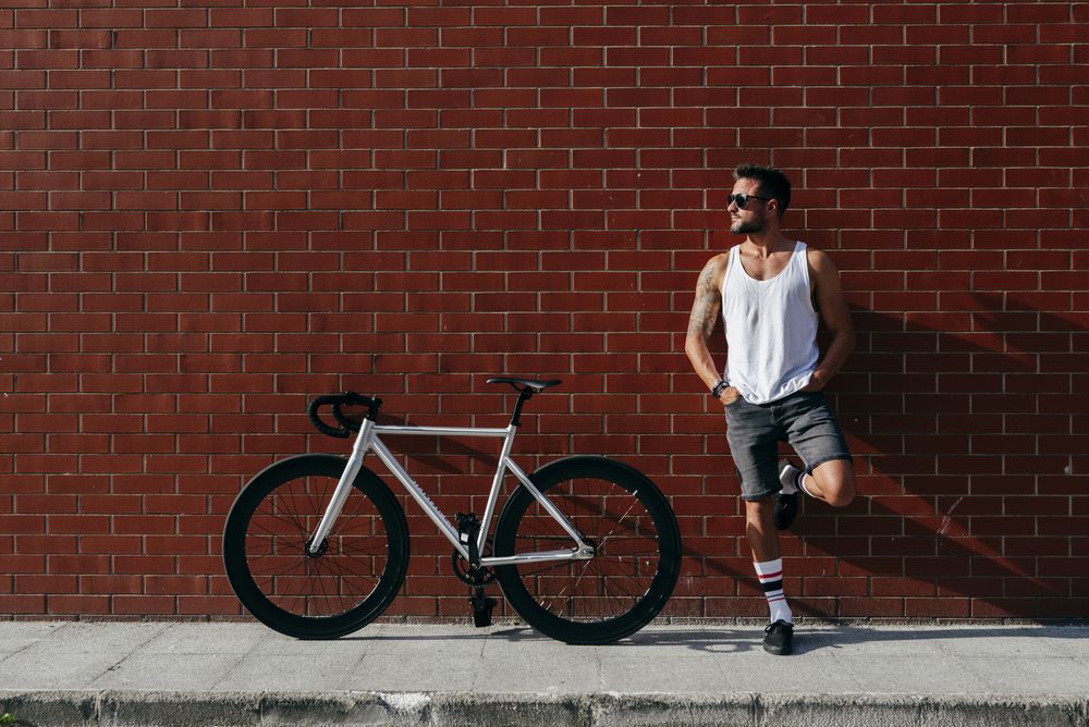 Sportive man standing next to brick wall with bike