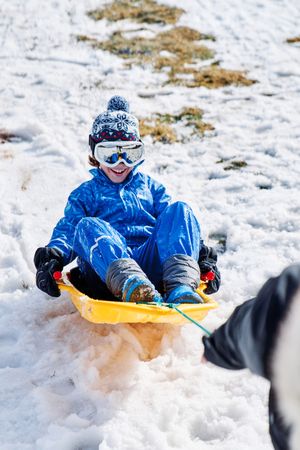 Crop parent pulling sleigh with glad son