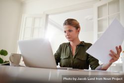 Portrait of young female sitting at table holding documents and working on laptop 4jjq84