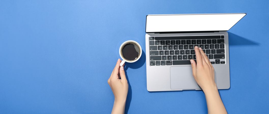 Looking down at person using laptop in a blue room with coffee with blank screen