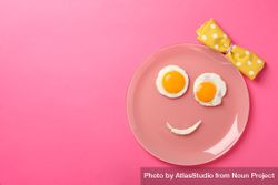 Looking down at pink plate with smiley face on it made of eggs and condiments, copy space 5XoVo0