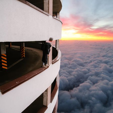 Person standing on balustrade above the cloud during sunset
