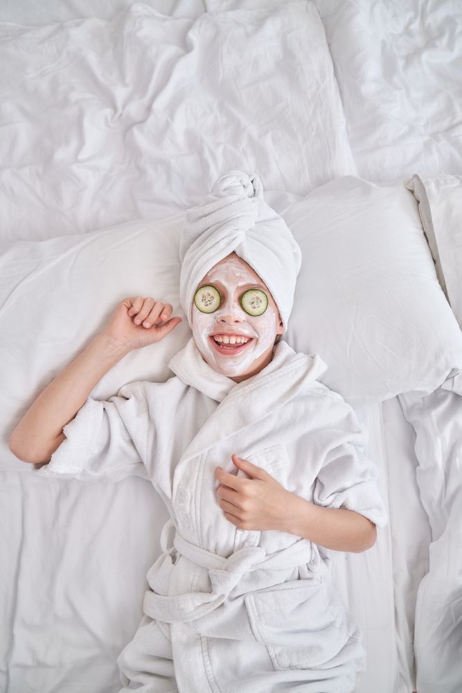 Kid in bathrobe and facial mask relaxing on bed at home