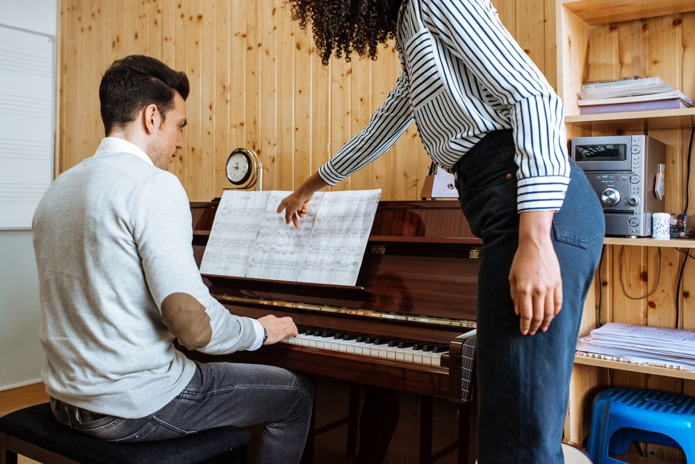 Man playing piano near woman teaching in studio