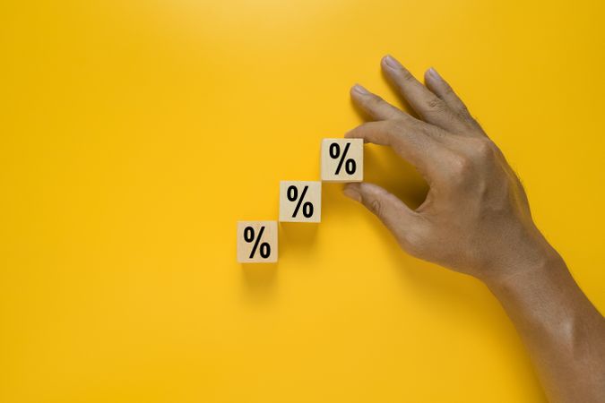 male hand put wooden blocks with percentage rate isolated on yellow background. concept of business growth or increasing interest rate